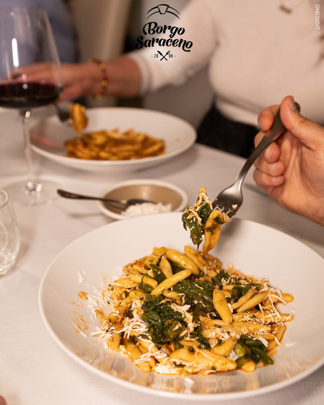 Cavatelli con verdure e formaggio grattugiato in piatto bianco, forchetta, calice di vino rosso da Borgo Saraceno