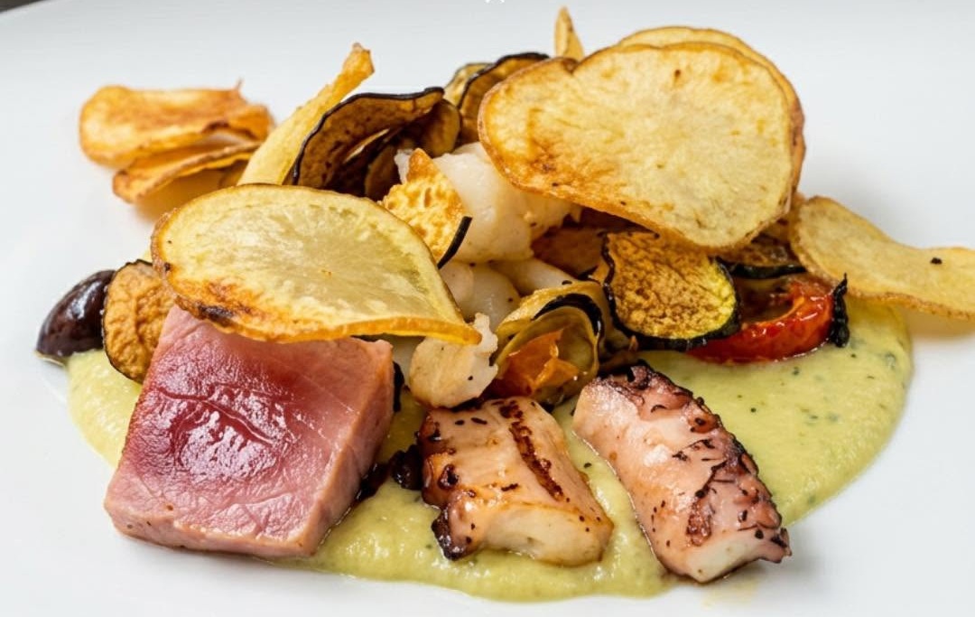 Tonno scottato e polpo arrostito su crema verde con chips di patate, melanzane grigliate e pomodoro in piatto bianco